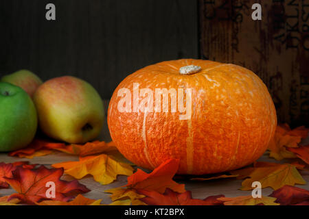 Orange Kürbis close-up auf einem Tisch, durch die Blätter im Herbst und Äpfeln umgeben. Thanksgiving, Harvest Festival. Stockfoto