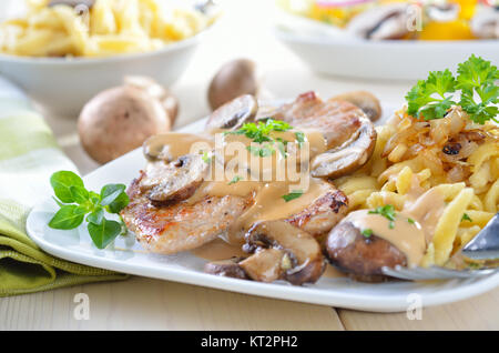 Schweineschnitzel mit Champignons, Sauce und Spätzle auf einem weißen auf einem weißen Teller serviert Stockfoto