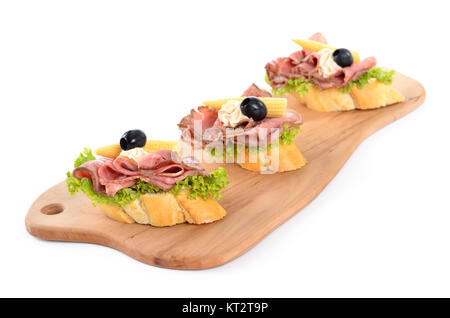 Baguette mit Roastbeef, kleine Maiskolben, Frischkäse und schwarzen Oliven auf einer hölzernen Schneidebrett Stockfoto