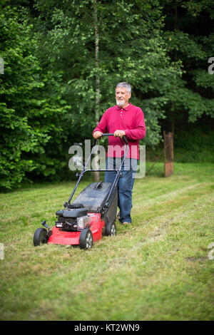 Senior woman Mähen des Rasens in seinem Garten Stockfoto