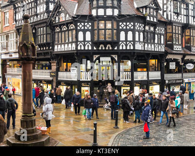 Weihnachten einkaufen zu Fuß über nasse Fahrbahnen und Kopfsteinpflaster in der römischen Stadt Chester England um die mittelalterliche Kreuz und die Geschäfte in den Zeilen Stockfoto