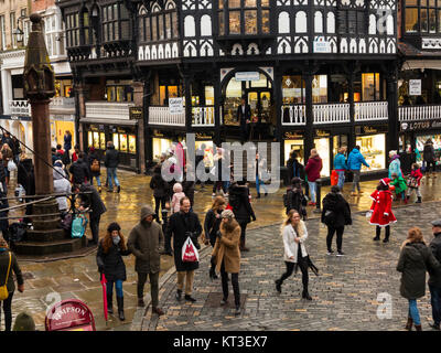 Weihnachten einkaufen zu Fuß über nasse Fahrbahnen und Kopfsteinpflaster in der römischen Stadt Chester England um die mittelalterliche Kreuz und die Geschäfte in den Zeilen Stockfoto