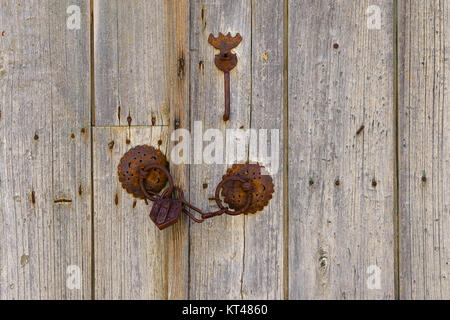 Nahaufnahme der rostigen alten Eisen Befestigungen mit Kette und Vorhängeschloss auf eine alte hölzerne Doppeltür, Griechenland. Stockfoto