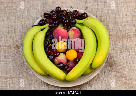 Ein hölzernes Schüsselchen von gemischten Früchten auf einem hölzernen Hintergrund, Banane, Kirschen, Pfirsiche Stockfoto