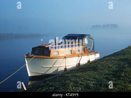 Kleine Motor Cruiser vertäut am Ufer des Flusses Bure, Norfolk, mit frühen Morgennebel Stockfoto