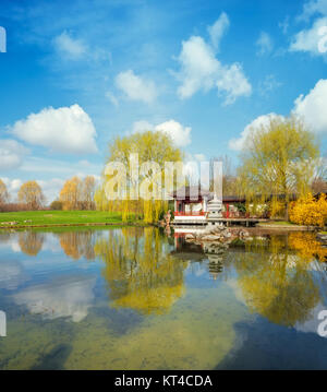 Stein Pagode im Teich von einem formellen Chinesischen Garten, Berlin, Deutschland. Konzentrieren Sie sich auf die steinernen Turm in der Mitte und die Gebäude Stockfoto