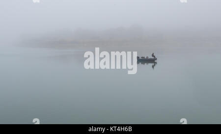 Fischer auf dem Boot in der Mitte des grossen Sees mit dichtem Nebel um ihn herum Stockfoto
