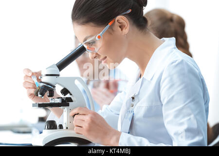 Seitenansicht des lächelnden Frau Nachwuchswissenschaftlerin arbeiten mit Mikroskop Stockfoto