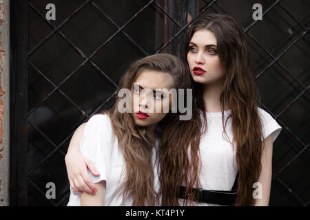 Zwei Angst horror Mädchen in Weiß Morgenmantel beiseite schaut erschrocken. Thema Halloween. Dunkles Bild von zwei schönen Angst ausblenden Mädchen mit geöffnetem Mund auf schwarzem Hintergrund. Stockfoto