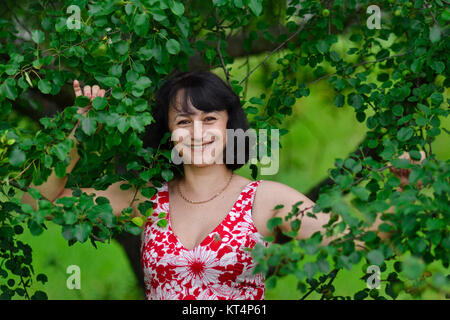 Die glücklichste Frau der Welt mit unglaublich schönen weißen Lächeln in grüne Bäume im Sommer. Schöne attraktive hübsche Frau mit weißen Lächeln stehen auf grün Hintergrund im Freien. Stockfoto