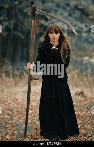 Schöne geheimnisvolle mystische Mädchen mit langen Haaren in schwarzem Kleid Holding ein Zopf in den dunklen Wald auf dem Weg. Mystische hübsches Mädchen in allen schwarze Kleidung mit Geflecht stehen in dunklen mystischen Wald Stockfoto