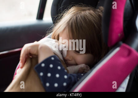 Ein Kleinkind Mädchen umarmt einen 6 Wochen alten Welpen, während in einem Kindersitz sitzen. Stockfoto