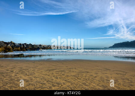 Wellenbrecher aus kubischen Steinen vor einem Sandstrand unter azurblauem Himmel Stockfoto