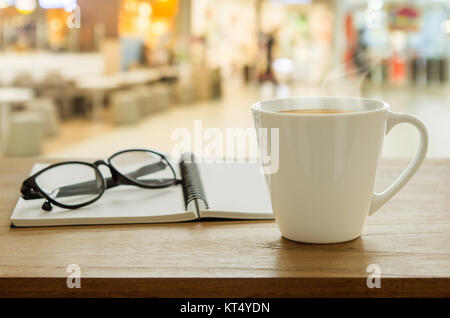 Tasse Kaffee, Brillen und Buch auf hölzernen Tisch in Coffee Shop. Stockfoto