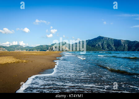 Wellen brechen und Umformen meer Schäume auf einen Sandstrand unter azurblauem Himmel Stockfoto