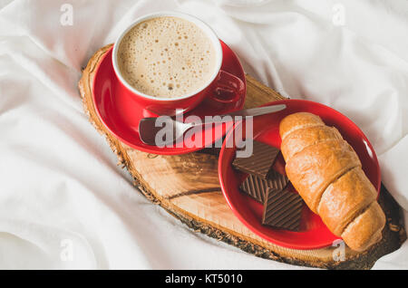 Cappuccino, Schokolade und Croissant auf einem Bett. Stockfoto