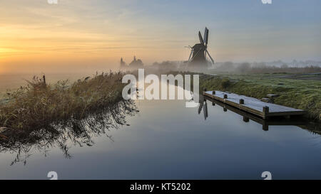 Landschaft der Windmühle in holländischen Polder entlang des Flusses am frühen Morgen Licht während der Nebel Sonnenaufgang Stockfoto