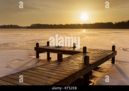 Orange Winter Landschaft mit See und Bootsanleger mit Eis in Bernsteinfarben Sunrise abgedeckt Stockfoto