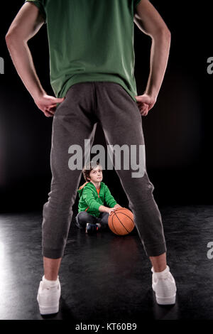 Junge am Boden mit Basketball Ball und sucht Mann im Vordergrund auf schwarz Stockfoto