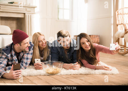 Glückliche junge Freunde auf Teppich und nehmen Selfie zu Hause liegen Stockfoto