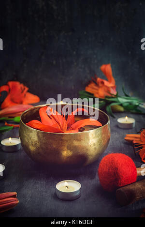 Tibetische Klangschale mit schwebenden in Seerose im Inneren. Spezielle Stöcke, brennende Kerzen, Lily Blumen und Blüten auf dem schwarzen Holz- Hintergrund. Medi Stockfoto