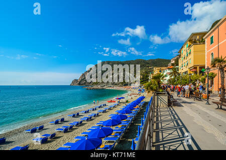 Der breite Sandstrand von Monterosso, Cinque Terre Italien mit Touristen, blaue Schirme und Stühle und das Ligurische Meer unter blauem Himmel Stockfoto