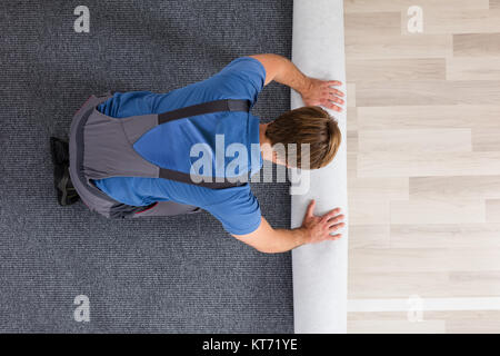 Männliche Arbeiter rollen Teppich auf dem Boden Stockfoto