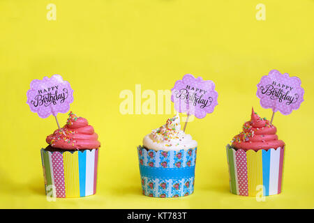 Drei leckere Erdbeere cupcakes in bunten Papier Backformen, mit Happy Birthday Grußkarte, auf gelben Hintergrund. Party Hintergrund Stockfoto