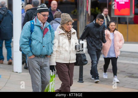 Senior Paar, man läuft durch eine Stadt einkaufen, in Hut und Mantel im Winter in Großbritannien gekleidet. Stockfoto