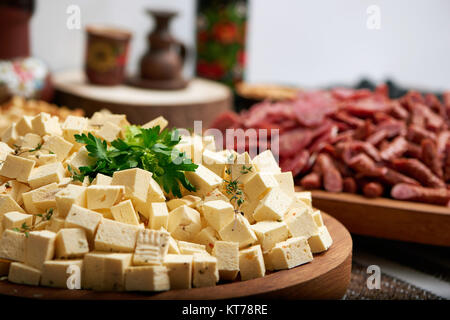 In der Nähe der großen hölzernen Platte, serviert mit wenig Käse Vorspeise Stücke und mit Petersilie dekoriert. Es gibt leckere Wurst auf der backgrou Stockfoto