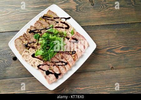 Nahaufnahme einer rechteckigen Platte voll von einem ausgestopften Fleisch, mit einem grünen Blätter und Sojasauce auf dem hölzernen Tisch eingerichtet. Stockfoto