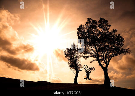 Glücklicher Fahrer halten Fahrrad und springen auf dem Hügel Stockfoto