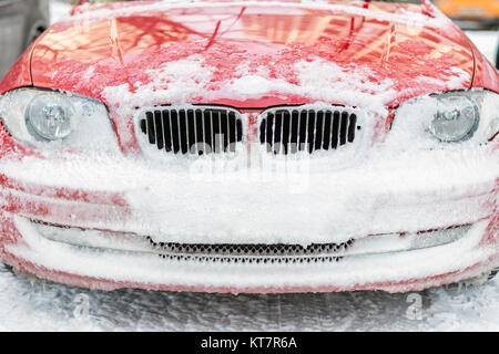 Vorne am Auto, Scheinwerfer, Motorhaube, Kühlergrill und Stoßfänger, mit Schnee auf einem Parkplatz abgedeckt Stockfoto