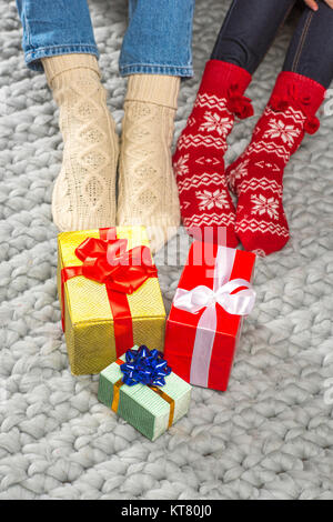 Beine in gestrickten Socken und Weihnachtsgeschenke Stockfoto