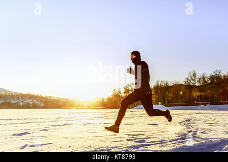 Sportler Läufer laufen auf Schnee in den Strahlen der untergehenden Sonne Stockfoto