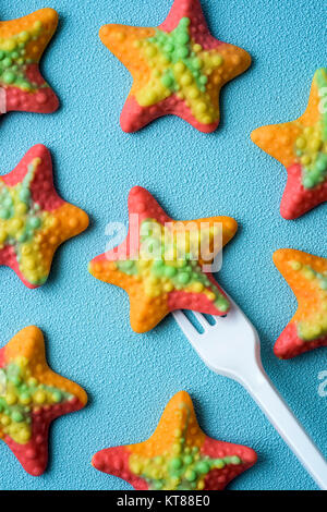 Hohe Betrachtungswinkel von starfish-förmige Gummibärchen Bonbons und einem Kunststoff Gabel auf einem blauen Hintergrund Stockfoto