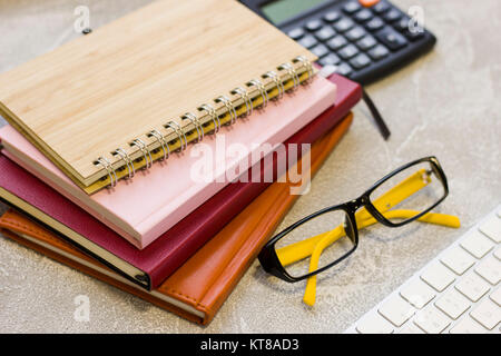 Ein Haufen von Notebooks und Planer, Gläser, eine Tastatur und einen Rechner an einem konkreten Hintergrund. Wirtschaft und Arbeit Konzept. Platz für Ihren Text Stockfoto