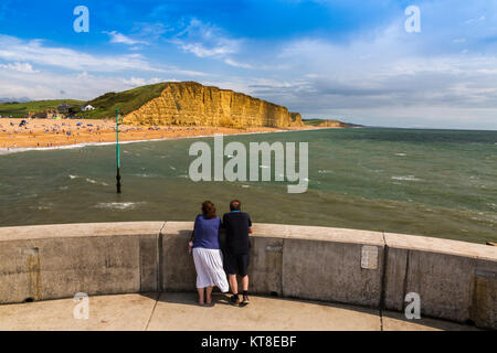Zwei Touristen die herrlichen geschichteten Sandstein von East Cliff mit einem riesigen Felsen fallen auf der Jurassic Coast West Bay in der Nähe von Dorset, England, Großbritannien Stockfoto