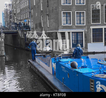 Mann stand auf Reinigung Barge angeln Wurf aus Kanal, Amsterdam, Holland Stockfoto