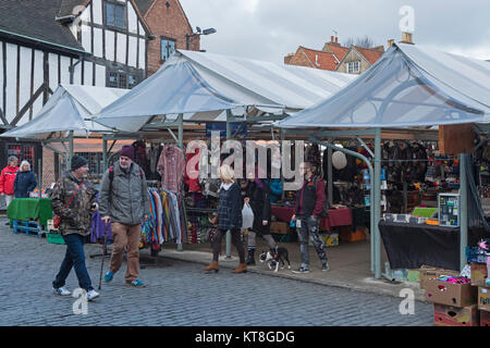 Menschen mit Tüten Spaziergang, vorbei an Ständen (1 Verkauf von Kleidung) in Trümmern, ein historischer Markt in York, North Yorkshire, England, UK. Stockfoto