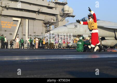 Ein U.S. Navy Matrose verkleidet als Weihnachtsmann, meldet eine F/A-18E Super Hornet Fighter auf dem Flugdeck der US Navy der Nimitz-Klasse Flugzeugträger USS Theodore Roosevelt Dezember 21, 2017 in den Arabischen Golf. Stockfoto