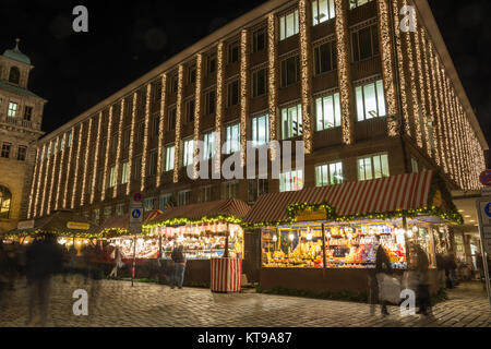 Nürnberg, Deutschland - Dezember 12th, 2017: Mehrere Stände auf dem Weihnachtsmarkt in Nürnberg während der Blauen Stunde vor einem Gebäude mit Weihnachten l Stockfoto