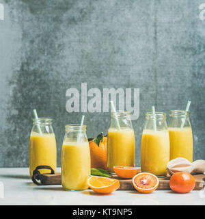 Gesunde gelbe Smoothie mit Zitrusfrüchten und Ingwer in Flaschen auf Holzbrett über Licht Marmortisch, selektiver Fokus, Kopieren, square crop. Cle Stockfoto