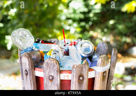 Eine hölzerne Mülltonne draußen im Park voll mit Plastik Flaschen, Dosen, Papier- und Plastiktüten. Stockfoto