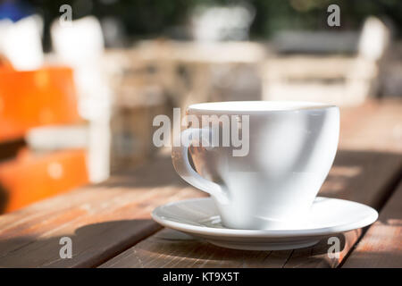 Eine Nahaufnahme eines weißen Tasse Kaffee mit einer Platte auf einem hölzernen Tisch im Freien, Sonne Licht. Stockfoto