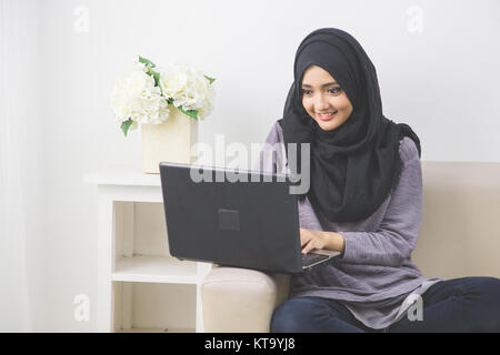 Attraktive junge Frau im Kopf scraf mit Laptop beim Sitzen auf der Couch Stockfoto