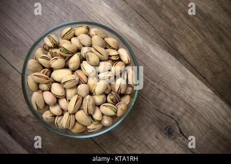 Glas Schale mit Pistazien auf Holz- Hintergrund Stockfoto