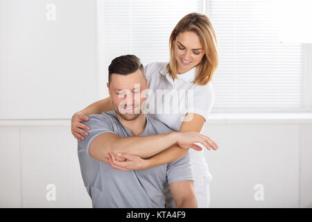 Lächelnd weibliche Physiotherapeut die Schulter Übung Stockfoto