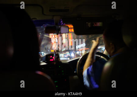 Taxi nach Chinatown, Bangkok. Ein Passagier ist im Außenspiegel der Fahrerseite wider, Treiber Bewegungen in Richtung der Leuchtreklamen, die Linie der Straße Stockfoto