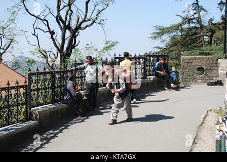 Ein Mann, der eine schwere Last auf dem Rücken durch die Straßen von Shimla. Stockfoto